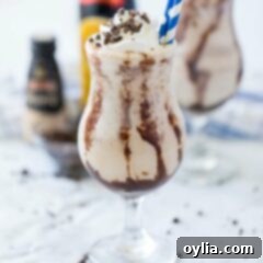 A glass of a luscious Frozen Mudslide cocktail with straws, garnished with chocolate.