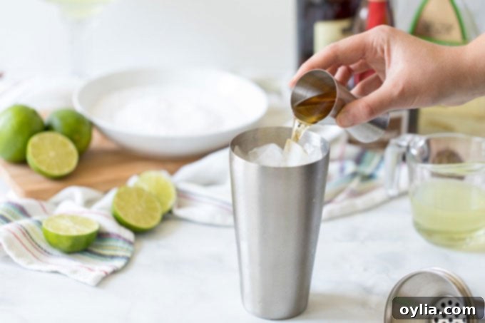 adding orange liqueur to a cocktail shaker with ice