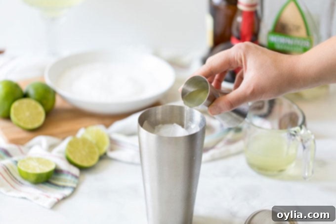 adding tequila to a cocktail shaker to make a margarita with other ingredients