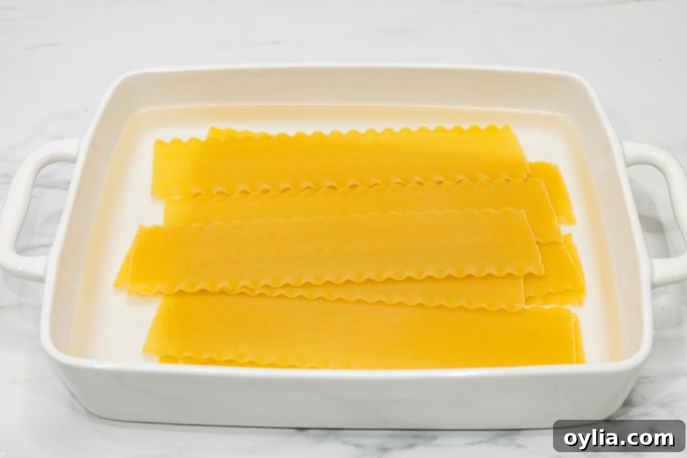 Lasagna noodles soaking in water in a baking dish