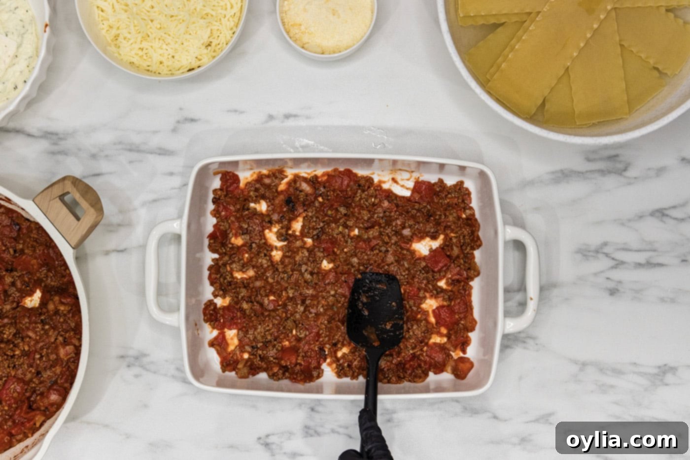Spoon spreading meat sauce mixture on bottom of baking dish