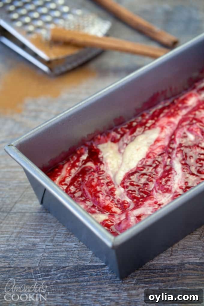 A loaf pan, expertly coated with cooking spray, now holding a layer of the coffee cake batter, topped with the luscious homemade raspberry filling.