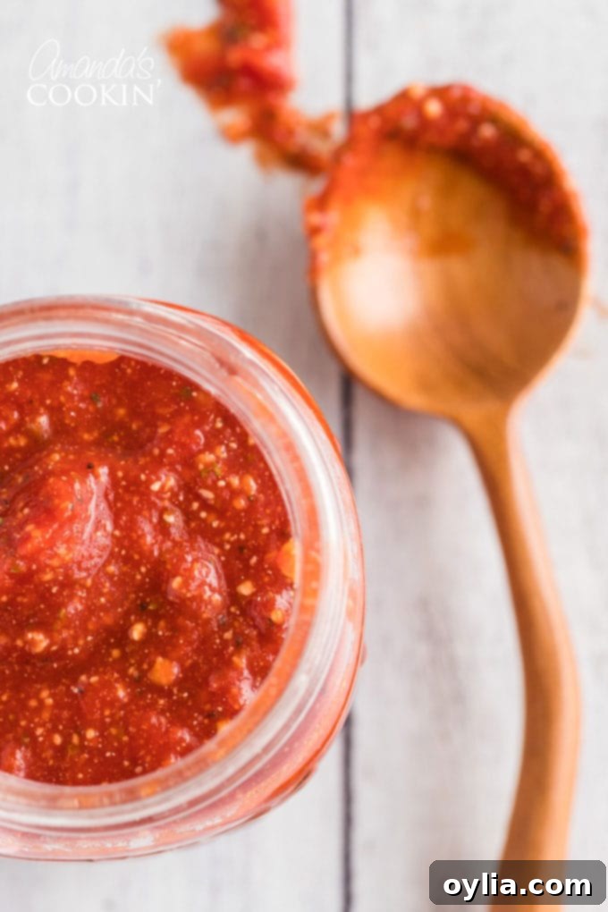 Close-up of a jar of rich homemade pizza sauce with a spoon resting beside it.