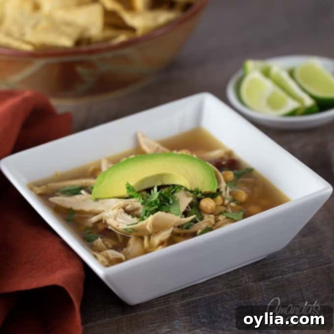 A white square bowl filled with chipotle chicken soup and topped with one slice of avocado.