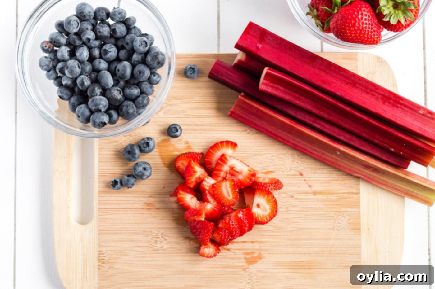 Bowl of blueberries, rhubarb and chopped strawberries on a wooden cutting board