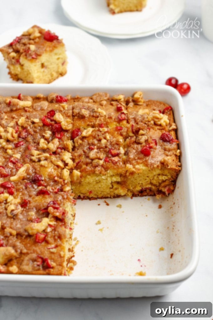 A 9x9 inch pan of baked cranberry streusel coffee cake with several squares already removed, showcasing its moist texture