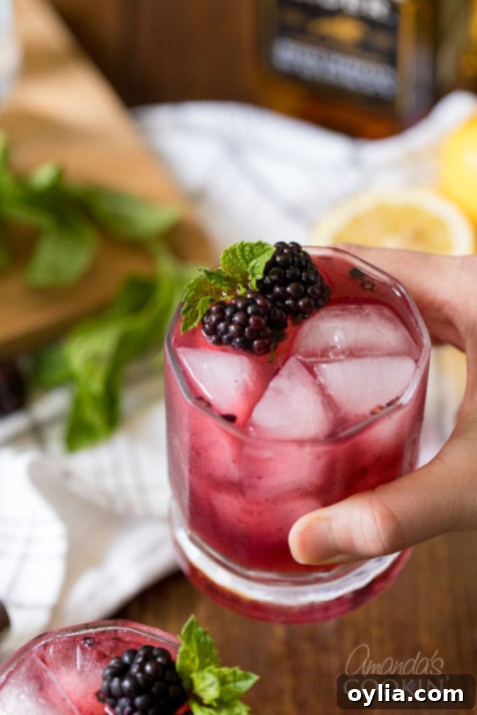 Midnight Berry Bourbon 8 hand holding a glass of blackberry bourbon lemonade cocktail with a blackberry garnish