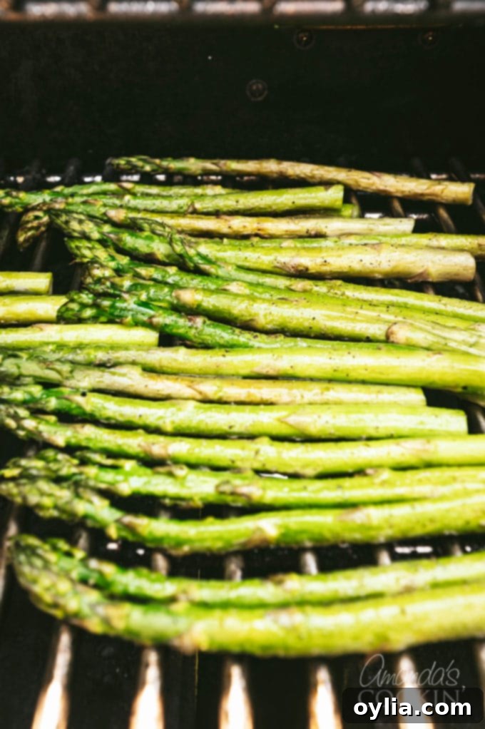 Fresh asparagus spears being placed directly onto the hot grill grates for cooking.