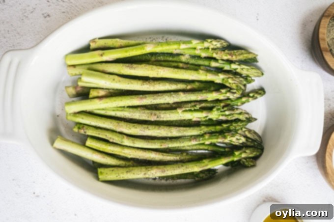 Asparagus in a shallow dish with small bowls of Kosher salt and freshly ground black pepper around it, ready for seasoning.