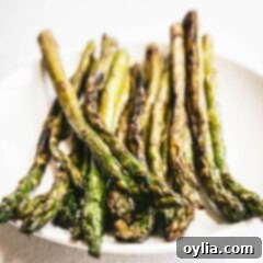 A close up of a perfectly grilled asparagus spear on a white plate with subtle char marks.