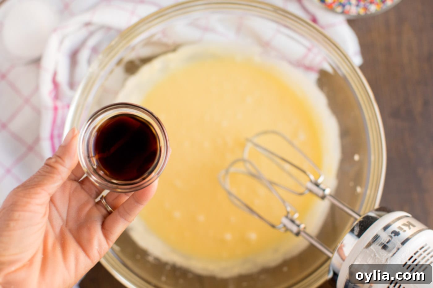 Smooth, pale yellow cookie batter being vigorously mixed in a bowl, showing the incorporation of eggs and anise extract for Italian Anisette Cookies.