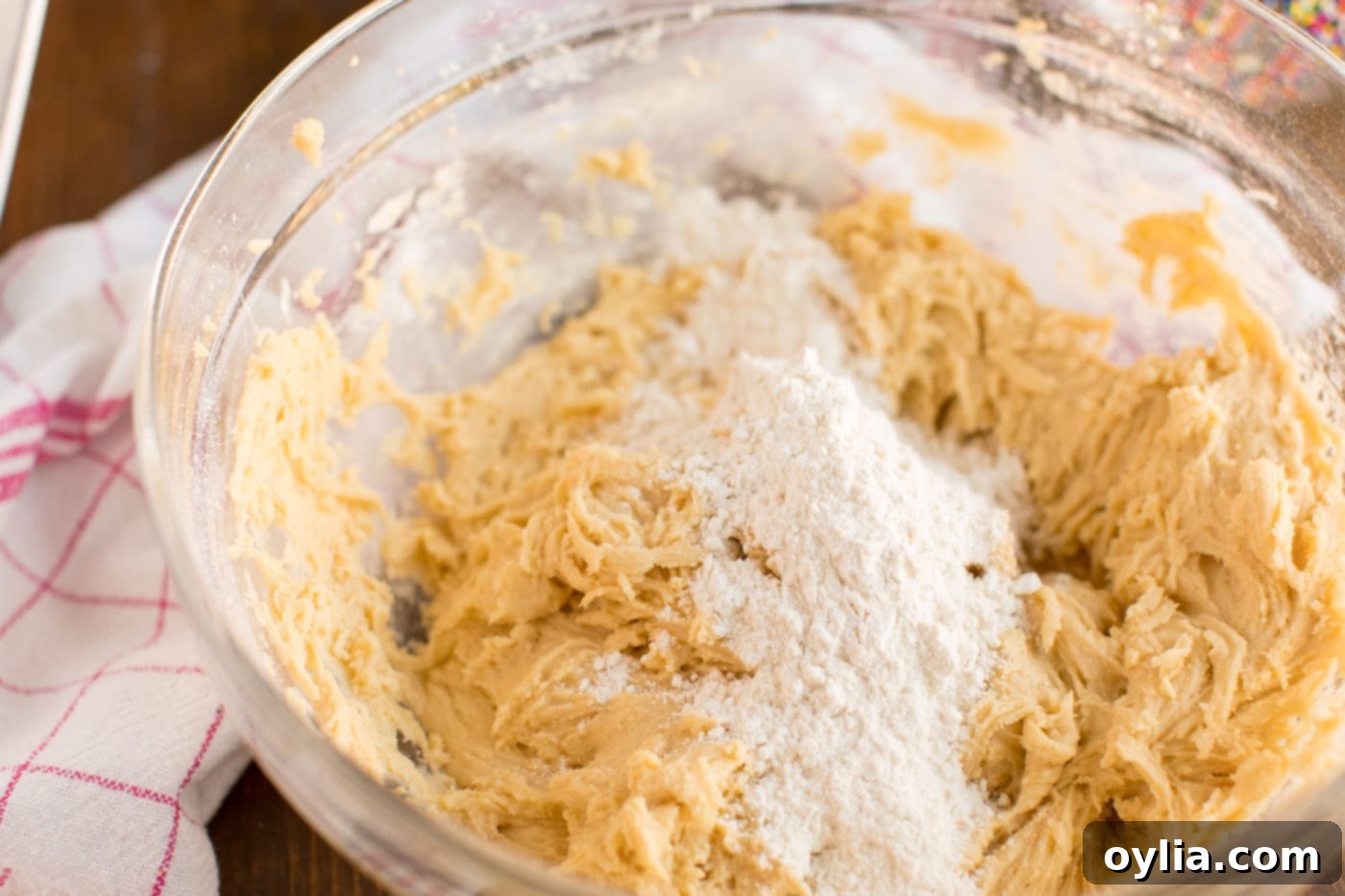 A baker's hands gently mixing soft cookie dough in a bowl, illustrating the perfect pliable consistency required for rolling perfect Italian Anisette Cookies.