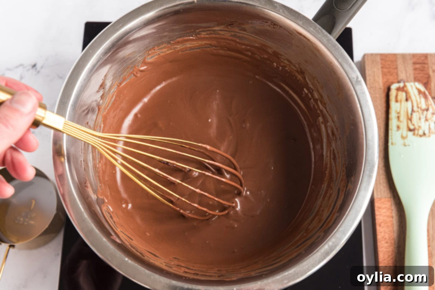 Milk and melted chocolate mixture in a bowl with a whisk, showing smooth consistency