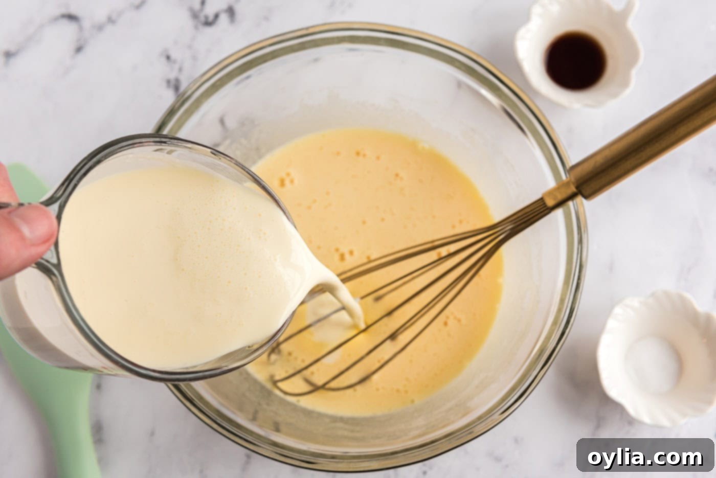 Pouring heavy cream into a bowl containing whisked eggs and sugar mixture