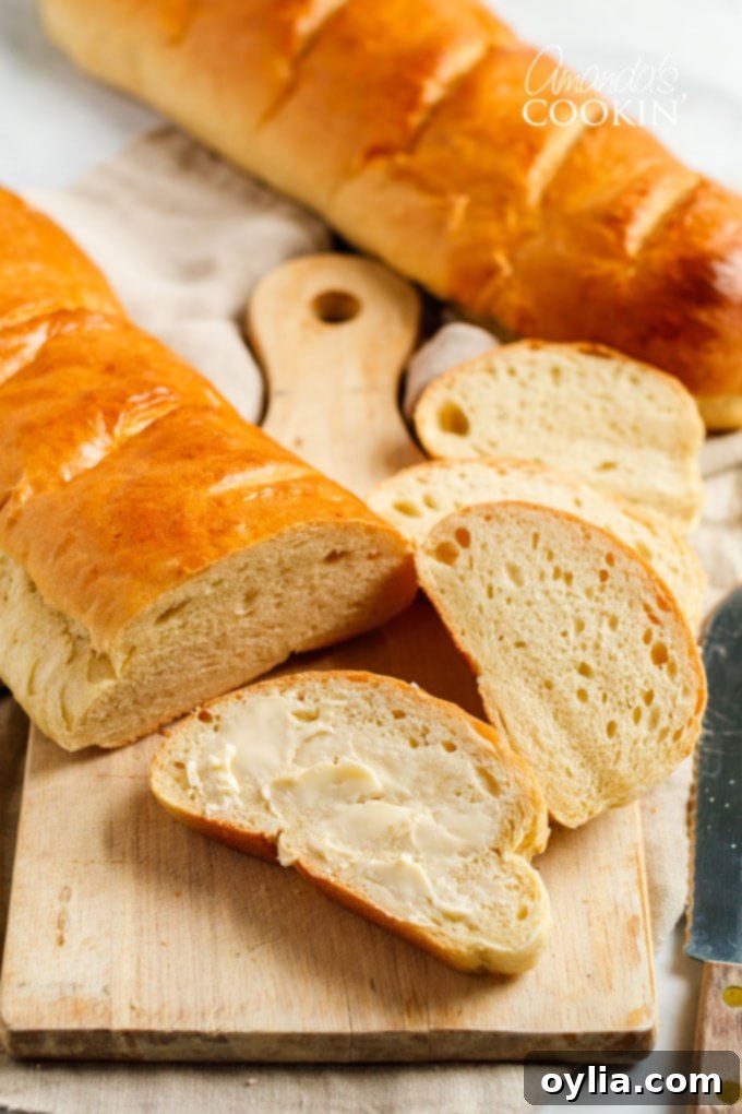 A rustic loaf of homemade Italian bread on a wooden cutting board, with a slice already buttered and ready to eat.