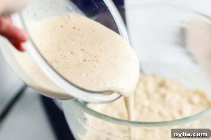 Adding the activated yeast mixture into the main bowl of bread dough ingredients.