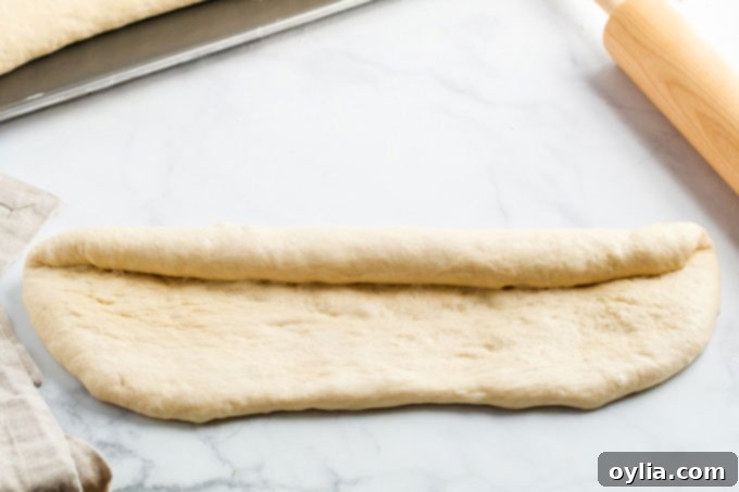 Chef rolling bread dough lengthwise into a jelly roll shape on a floured countertop for shaping.