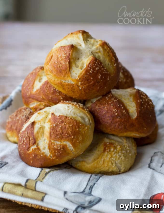 A stack of perfectly golden brown pretzel buns laying on a towel.