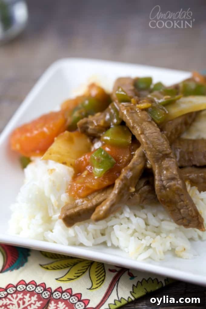 A close up of a white plate with rice and Chinese pepper steak on top.