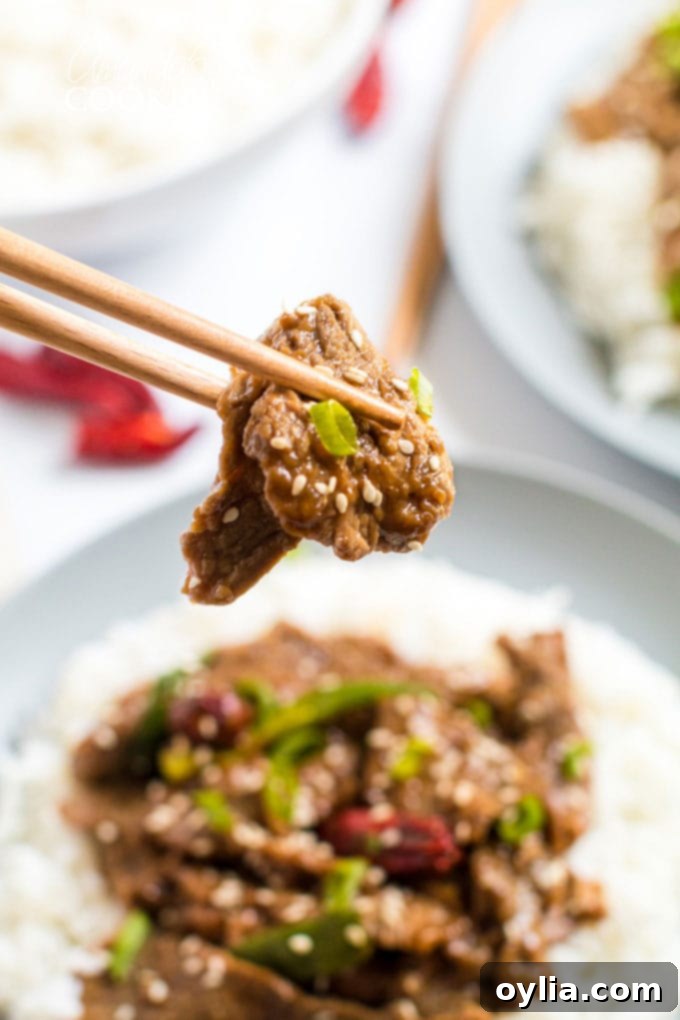 Chopsticks holding a piece of tender Mongolian Beef with green onions.