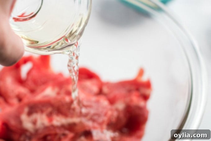 Sherry cooking wine being poured over thinly sliced beef and cornstarch in a bowl for marination.