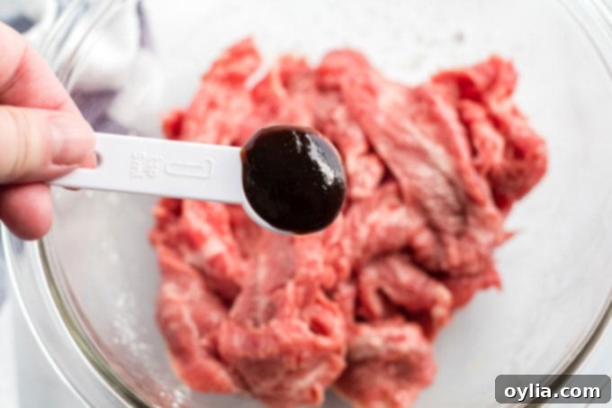 Adding a teaspoon of hoisin sauce to marinated beef in a bowl.