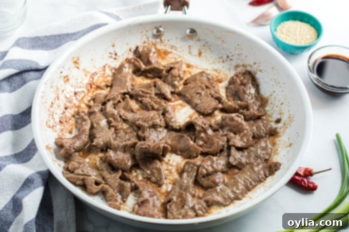 Thinly sliced beef stir-frying in a hot skillet, searing to a golden brown.