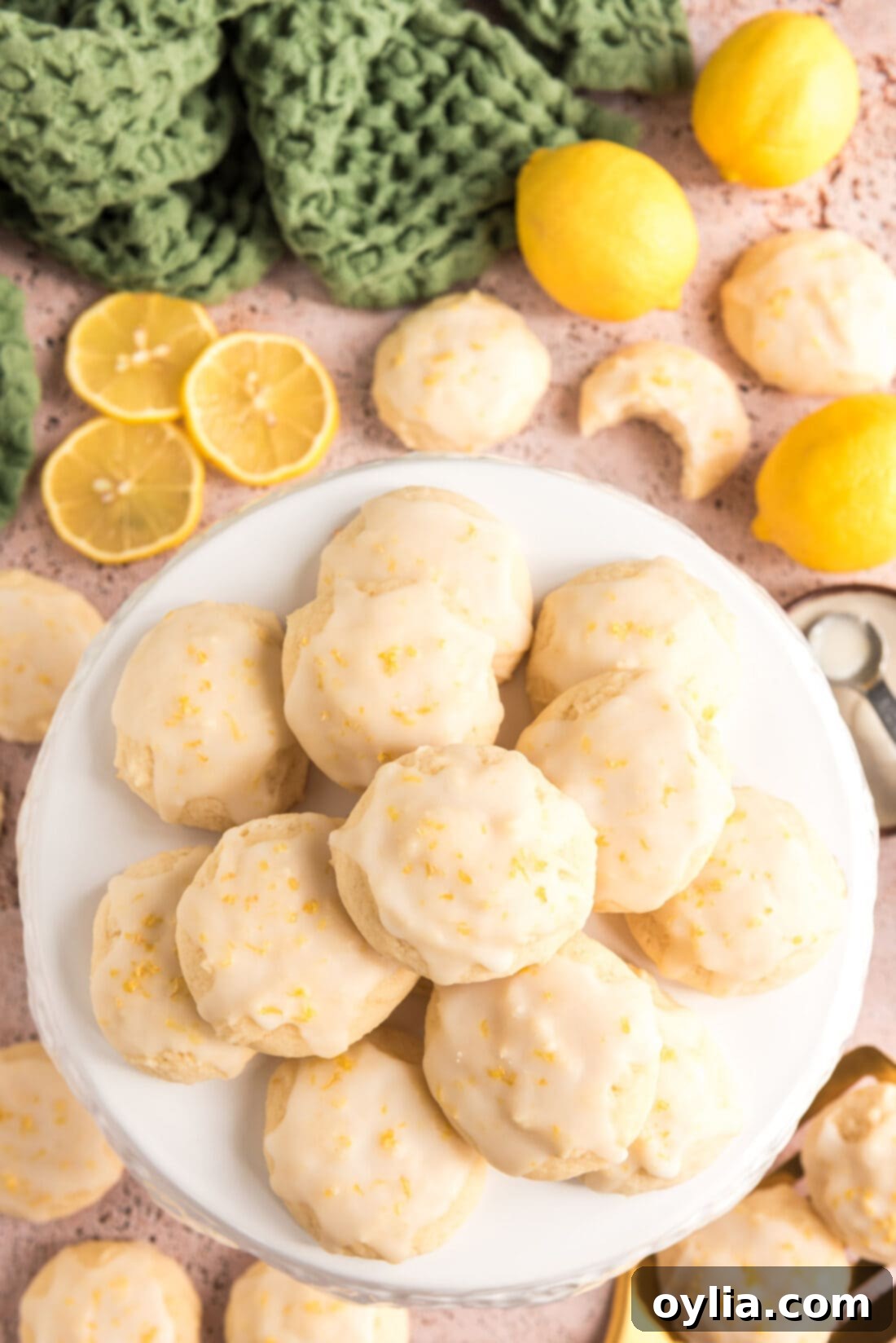 Piled high Lemon Drop Cookies with a bright yellow glaze on a white plate, showcasing their inviting texture and delicious appearance.