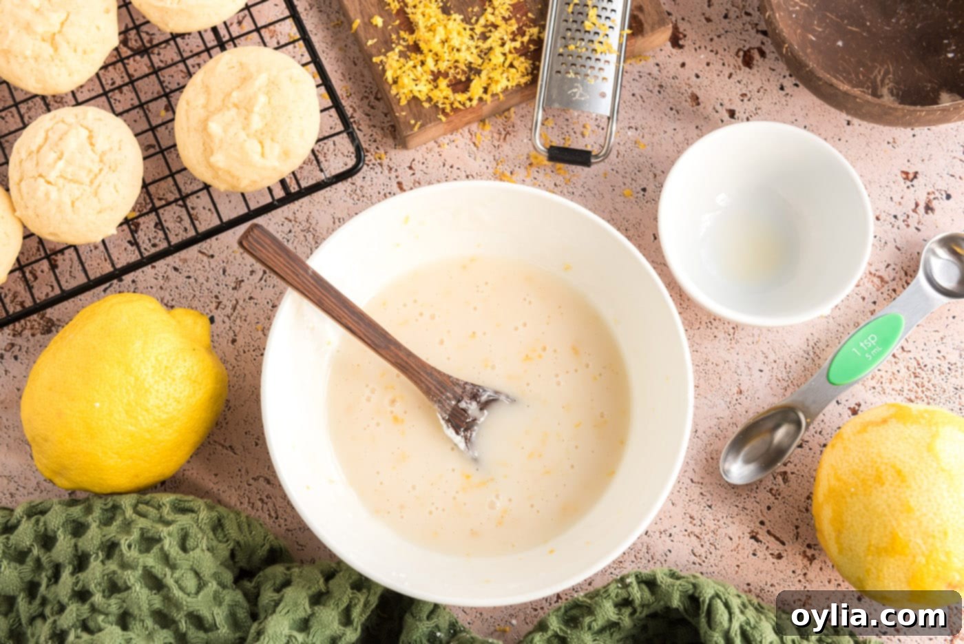 A small bowl of freshly prepared lemon glaze, smooth and bright yellow, with visible flecks of lemon zest.