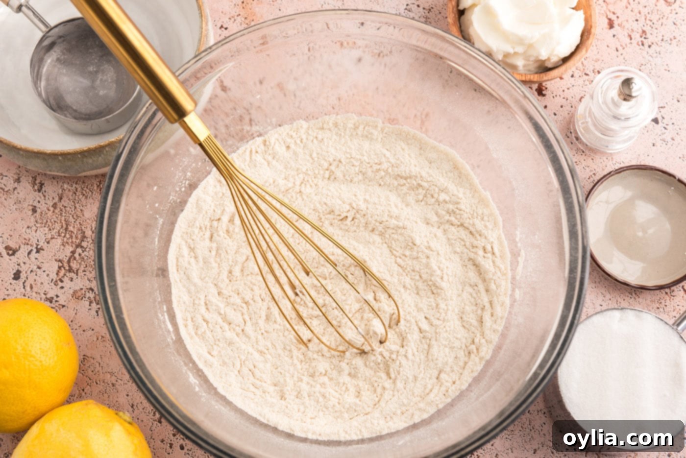 A white bowl containing sifted flour, baking powder, and salt with a whisk resting in it, ready for use in baking.