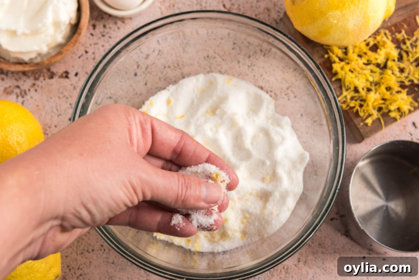 Hands actively rubbing bright yellow lemon zest into white granulated sugar in a mixing bowl, demonstrating the flavor infusion technique.