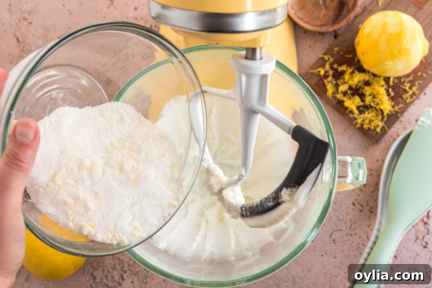 Shortening being creamed in a stand mixer bowl, with the fragrant lemon-sugar mixture being slowly added.