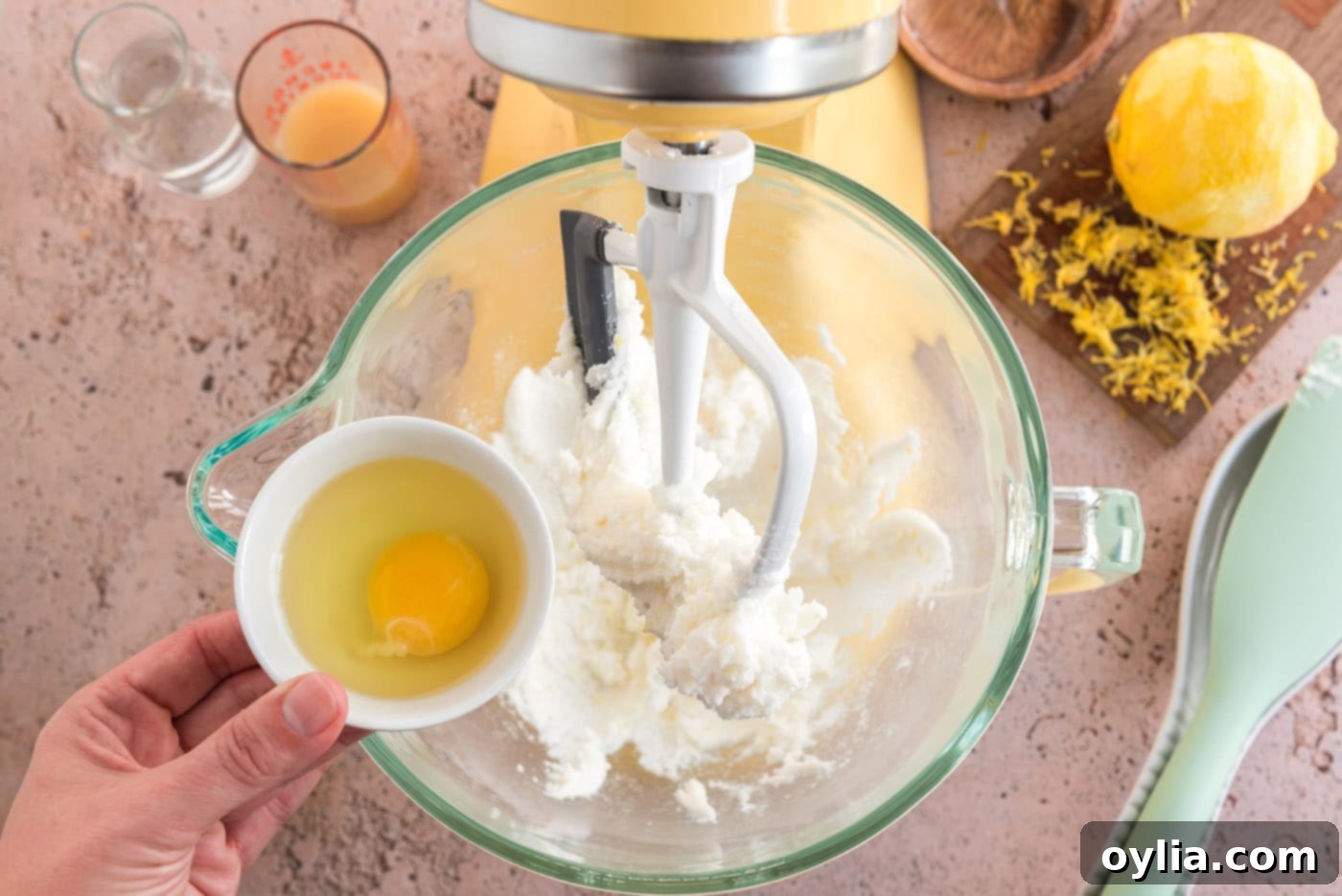 A hand cracking a large egg into the lemon cookie batter in a mixer bowl.