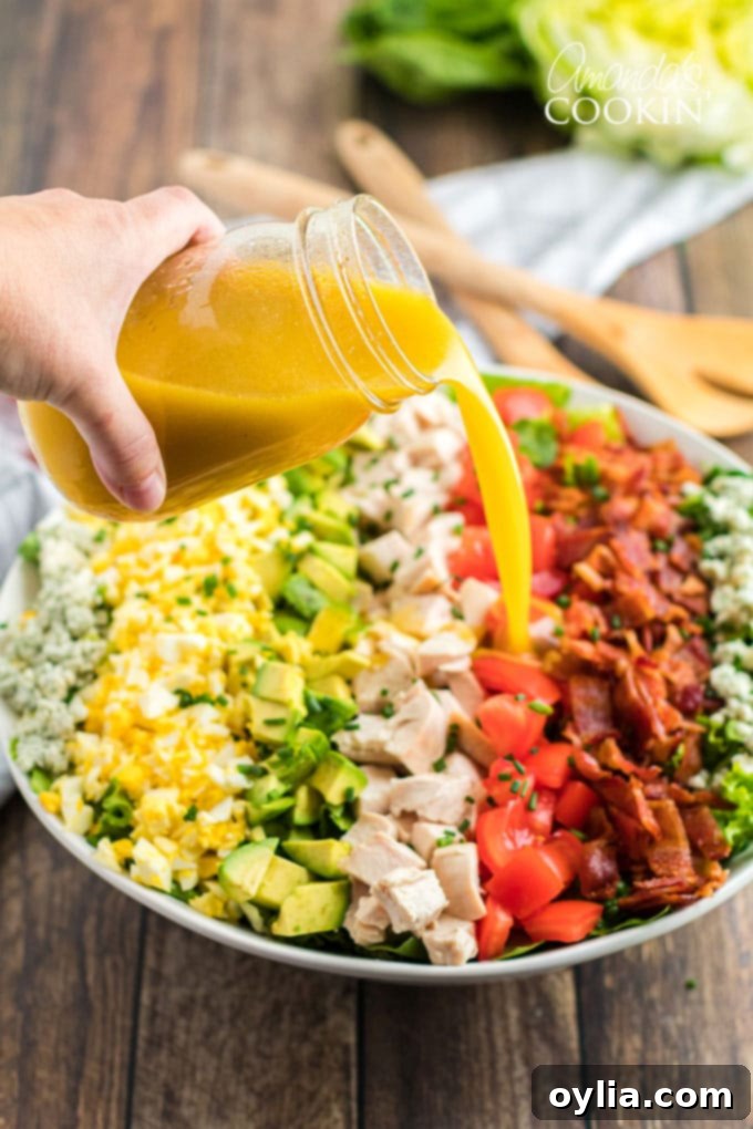 Hand pouring dressing over a colorful Cobb Salad