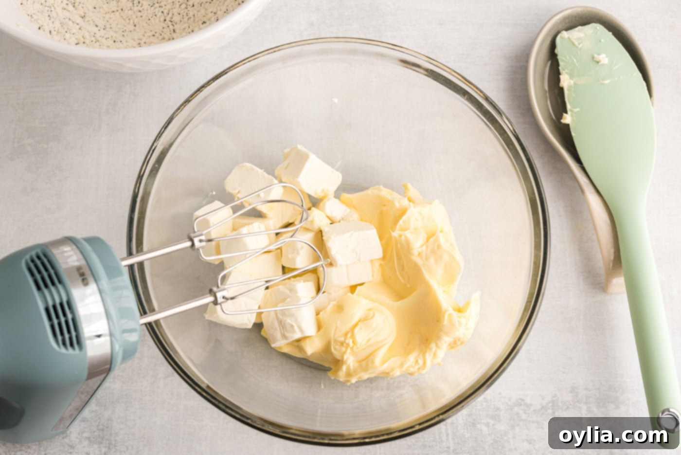 butter and cream cheese being beaten in a bowl with a handheld mixer until creamy