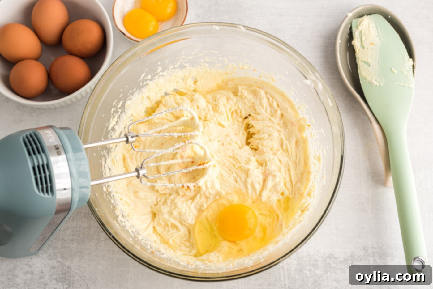 eggs being added to a bowl of orange poppy seed pound cake batter and mixed