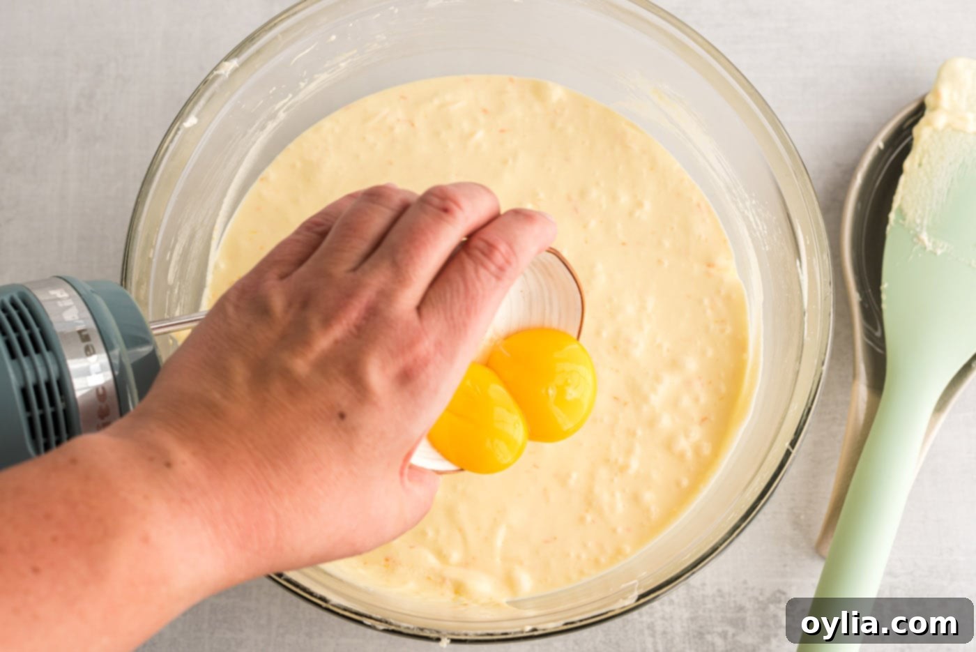 hand pouring egg yolks into pound cake batter, mixing well