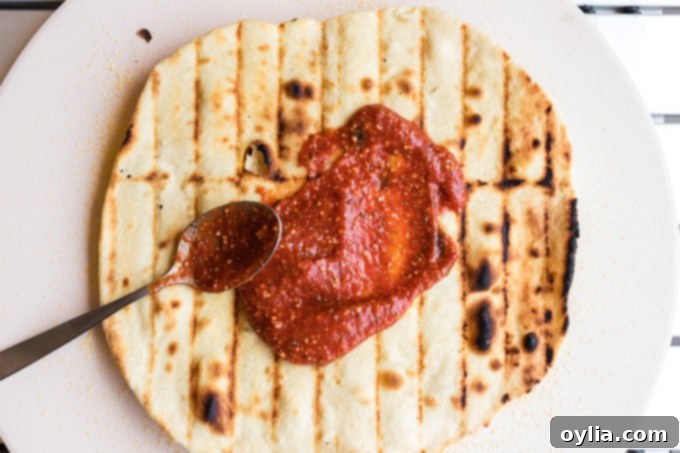 spreading sauce on grilled pizza dough