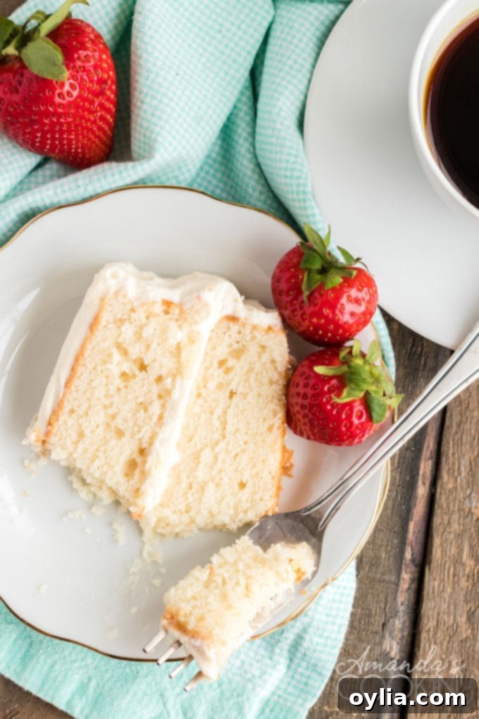 Only 8 ingredients needed for this fluffy white cake recipe that bakes up in just 30 minutes! Perfect for a party, in layers, or baked as a sheet cake! slice of white cake on a plate with strawberries and a fork
