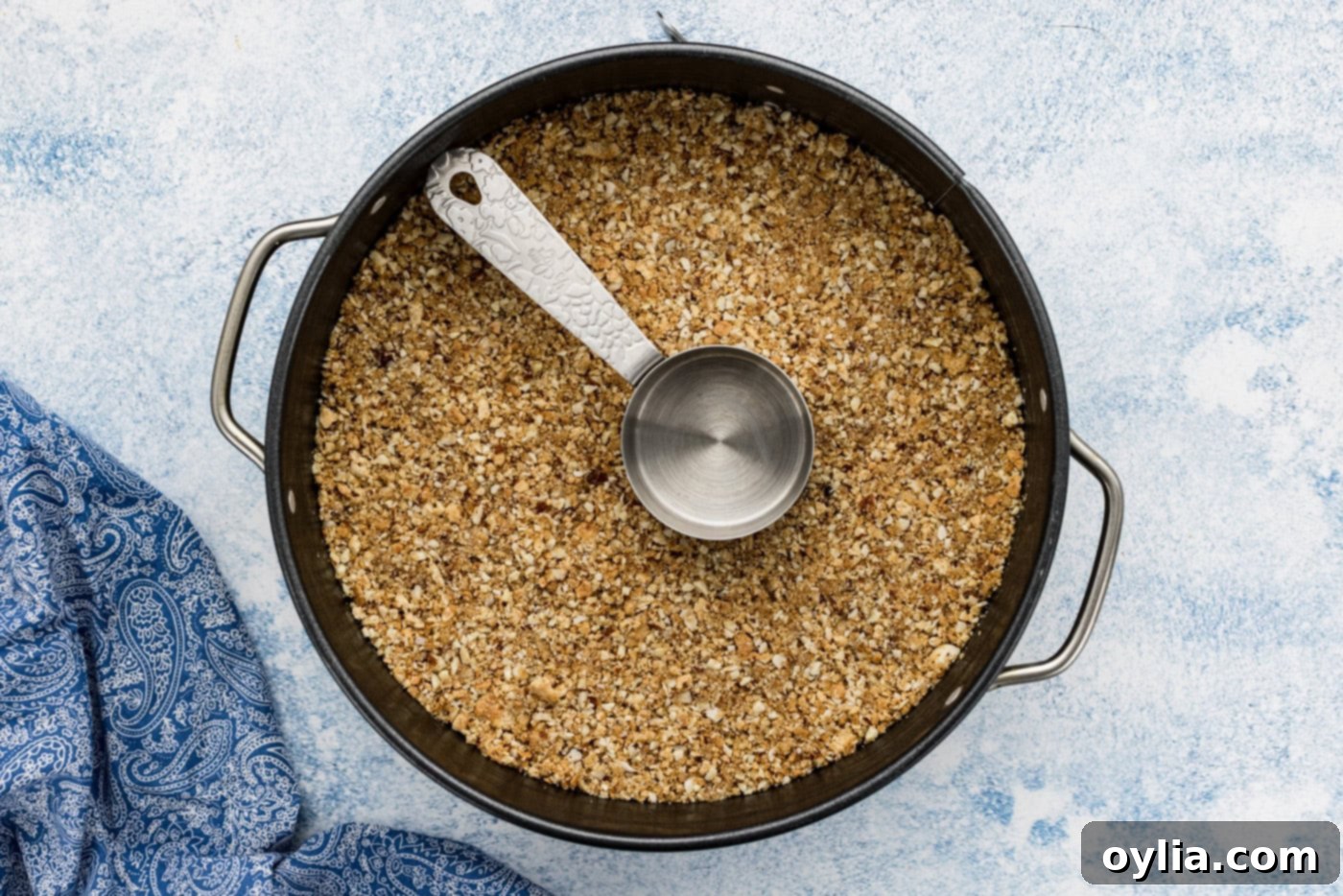 measuring cup pressing down almond graham cracker crust in a pan