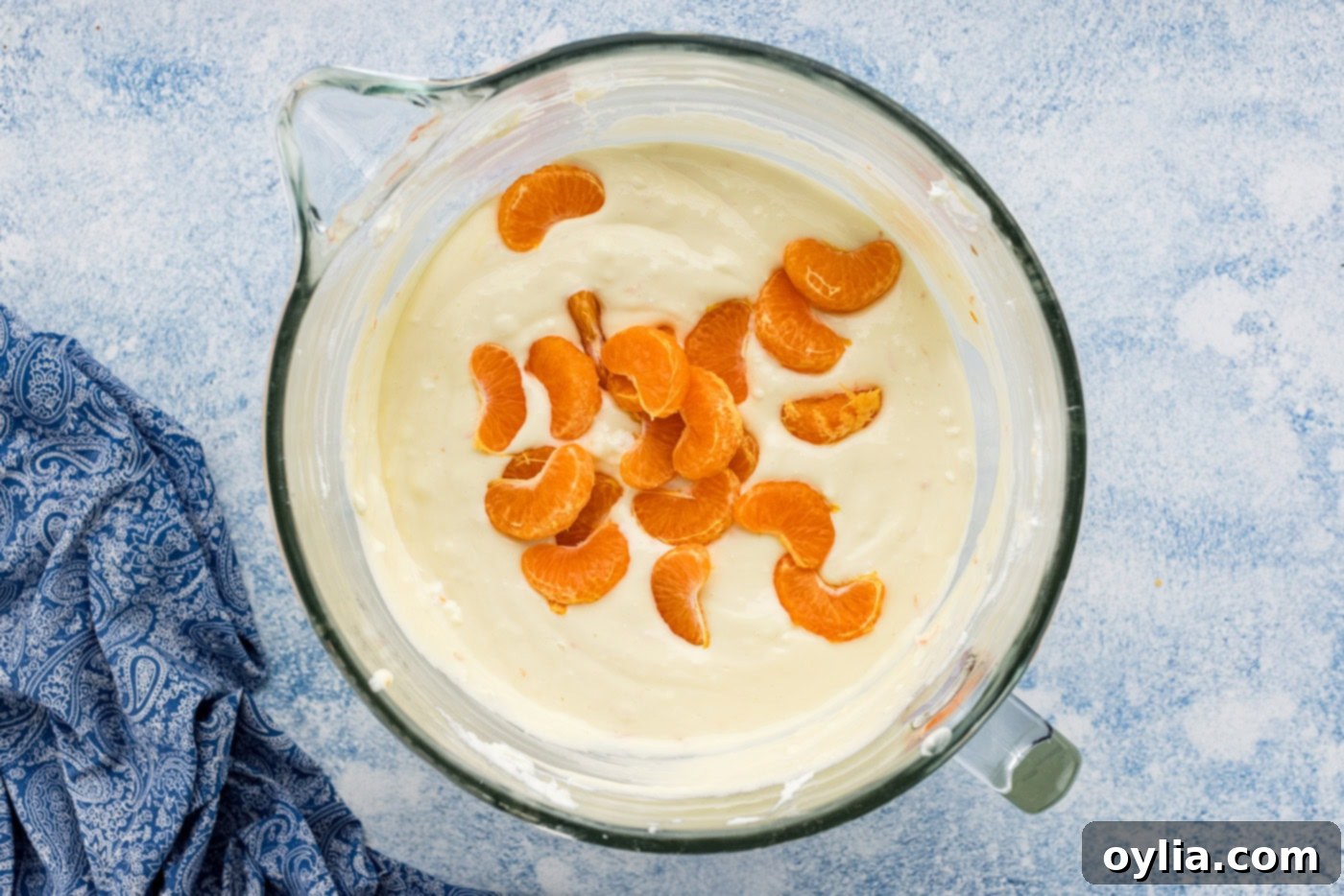 mandarin orange slices added to cheesecake batter in a bowl