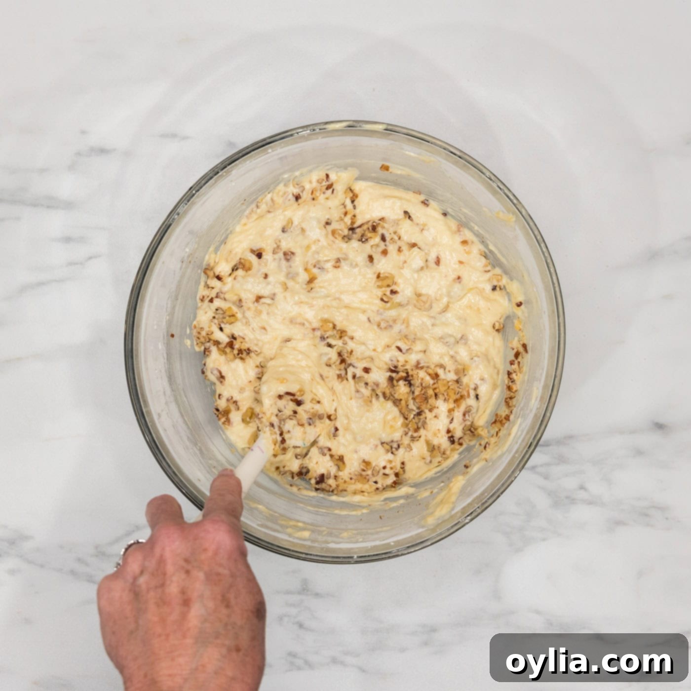 stirring walnuts into bundt cake batter in a bowl