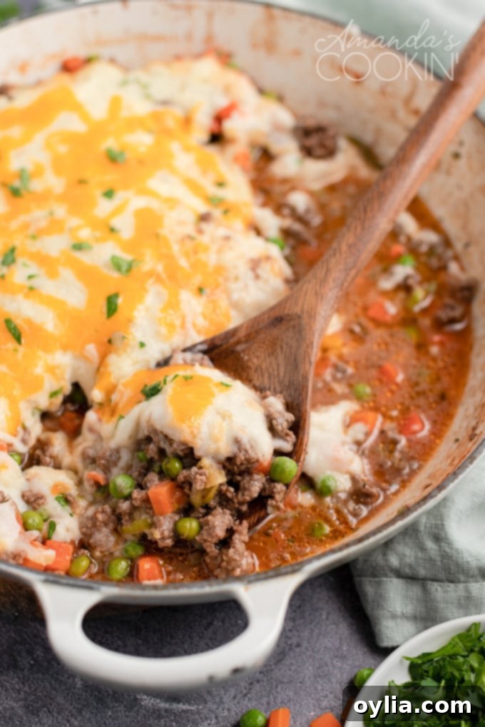 Spoon lifting a generous portion of classic Shepherd's Pie from a pan, showing the golden mashed potato topping and rich meat filling.