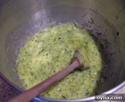 An overhead photo of a bowl containing shredded zucchini, vegetable oil, eggs, and vanilla, ready to be mixed for zucchini bread.