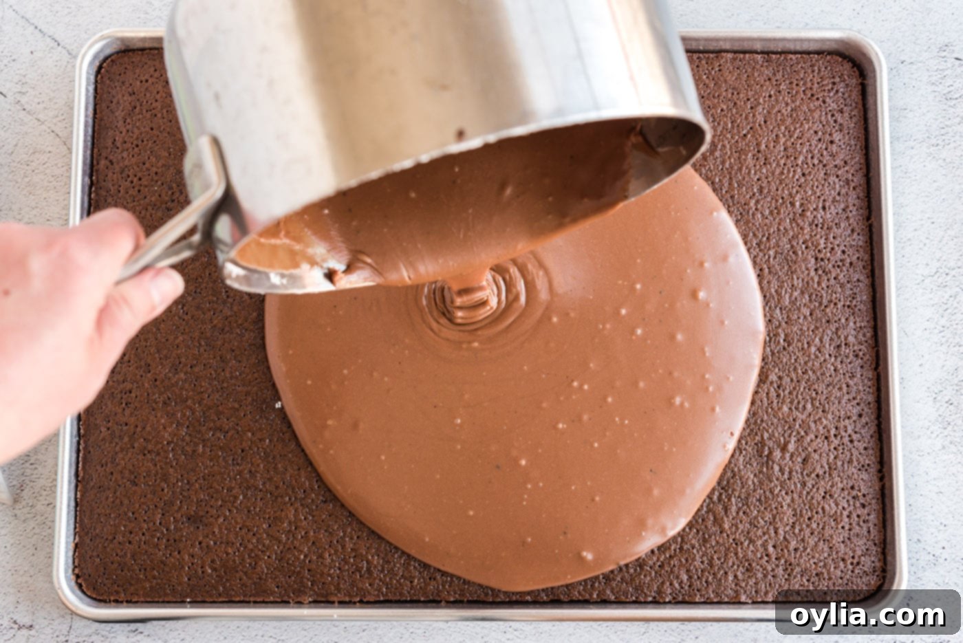 Pouring hot chocolate icing over the freshly baked, warm chocolate sheet cake