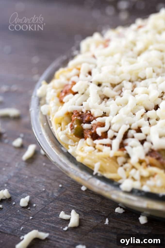 A close up of a clear pie pan filled with spaghetti pie with mozzarella cheese on top.