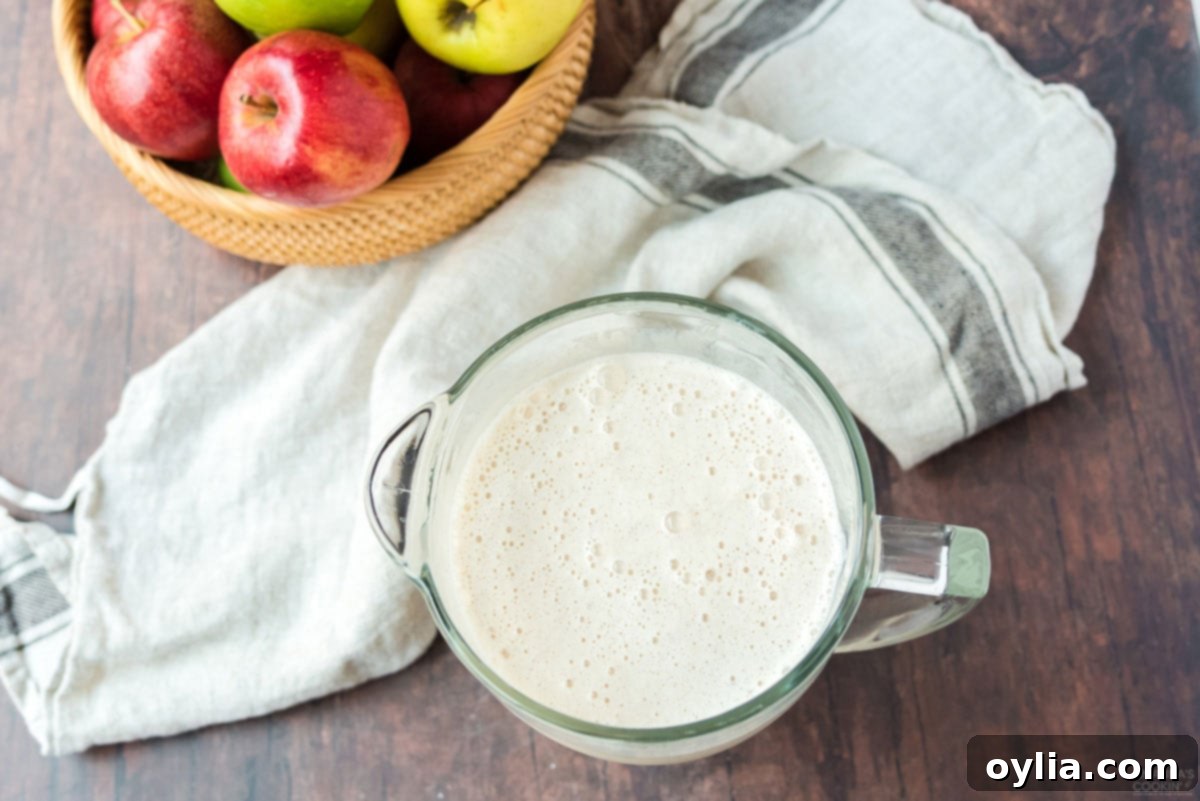 A measuring cup filled with a perfectly blended apple cider milkshake, showcasing its creamy and smooth texture.