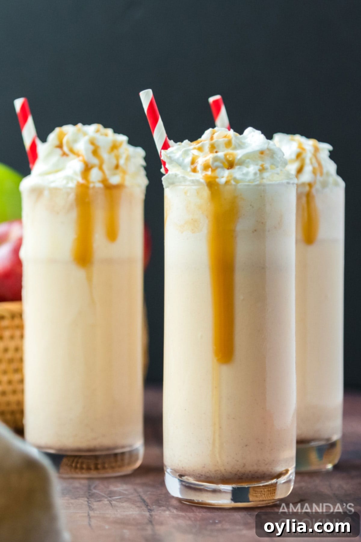 Three beautifully presented apple cider milkshakes, each in a tall glass, adorned with whipped cream, cinnamon, and festive straws, ready to be enjoyed.