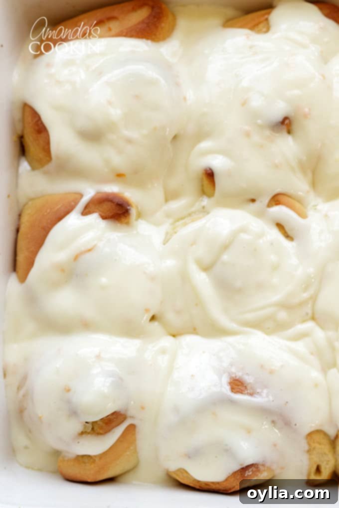 Freshly baked orange rolls covered in a generous layer of creamy, bright orange frosting, still warm in the baking dish.