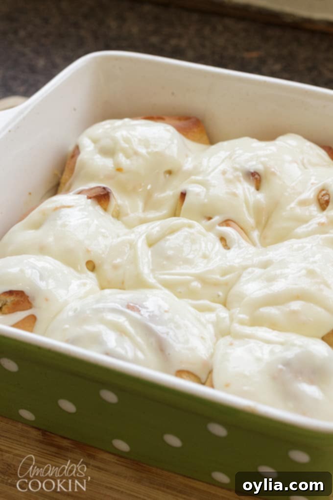 A pan of delectable orange rolls, now fully frosted with a rich cream cheese glaze, glistening and ready to be served.